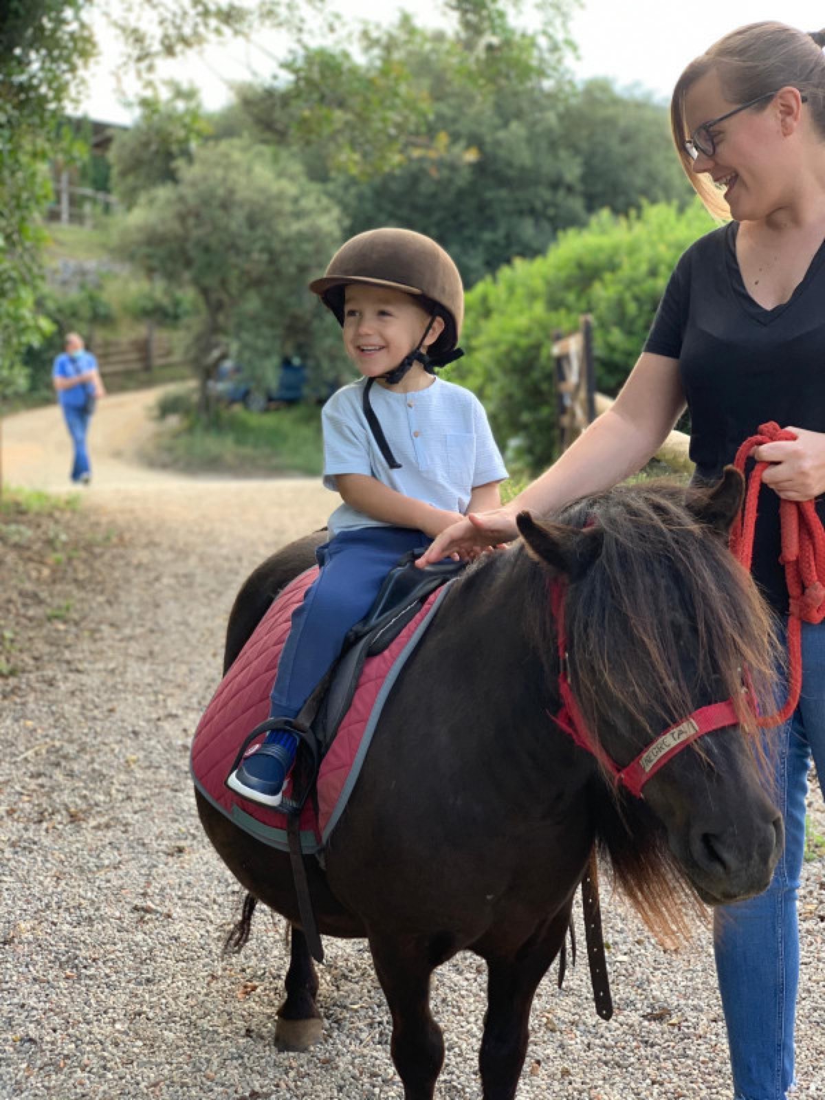 Niño con casco montando un poni acompañado por una adulta